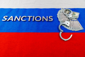the word sanctions laid with silver metal letters on russian tricolor flag near dollar banknotes...