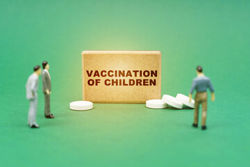 On the green surface are pills, miniature figures of people and a sign with the inscription - vaccination of children