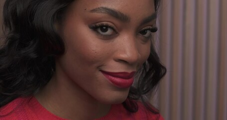 Close up on a beautiful black woman's face adjusting her hair behind her ears and then looks to camera and smiles.