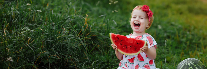 Banner little girl in a dress eats a watermelon at a picnic. - obrazy, fototapety, plakaty
