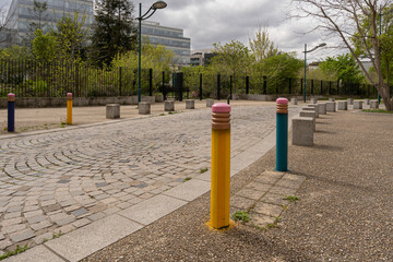 Gennevilliers, France - 04 06 2022: View of a paved road a pedestrian crossing a colored poles a park entrance and building behind
