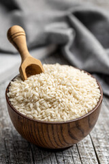 Uncooked Carnaroli risotto rice in bowl on wooden table.