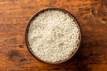 Uncooked Carnaroli risotto rice in bowl on wooden table.