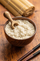 Uncooked Carnaroli risotto rice in bowl and wooden scoop.