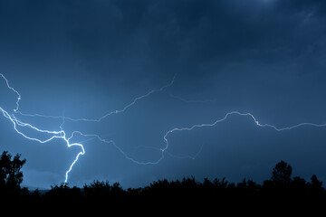 Electrical discharges during a summer storm, branched lightning bolts in the night sky.