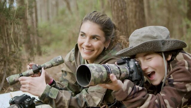 Happy Caucasian woman and her son taking photos in nature. Cheerful mother holding spy pipe while boy taking pictures of wildlife with professional camera. Nature, photography concept