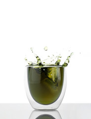 Glass of water with chlorophyll extract against white grey background. Liquid chlorophyll in a glass of water with splash. Concept of superfood, healthy eating, detox and diet, copy space, vertical