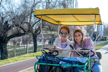 Fototapeta na wymiar Mother and daughter having fun riding a roofed tandem bicycle or a quadricycle with a steering wheel on a promenade.