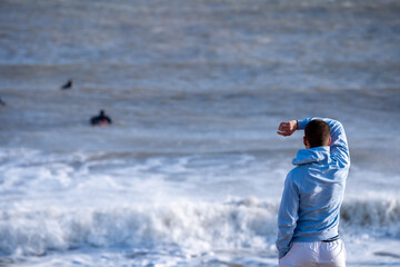 Rear view of a young man on the beach at Rivedoux watching surfers riding the waves, Ile de Ré, Re...