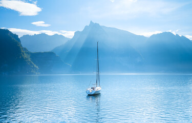 A yacht against the backdrop of the mountains in Switzerland. Calm water and bright sunny day. A popular place to travel and relax.