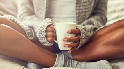 Weekend bliss. Shot of an unidentifiable young woman enjoying a cup of coffee while sitting on her couch at home.