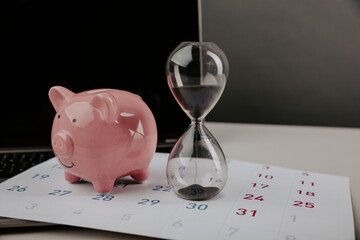 Hourglass with piggy bank on a calendar with laptop close-up. Online business concept