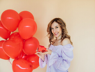 A young woman with heart-shaped balloons and a gift box. The concept of the holiday on March 8 and Valentine's Day.