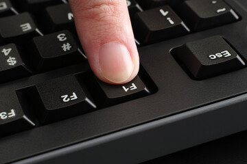 Ein Finger, der die Taste F1 auf einer schwarzen Computertastatur drückt