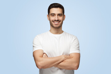 Attractive man in white t-shirt stands with crossed arms isolated on gray background