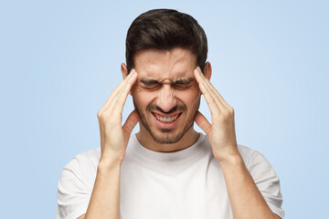Attractive young man suffers from severe headache pressing fingers to temples - obrazy, fototapety, plakaty