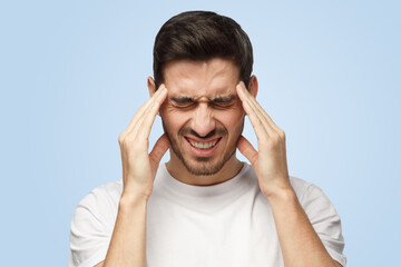 Attractive young man suffers from severe headache pressing fingers to temples