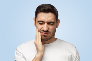 Attractive young man feels pain holding his cheek with hand suffering from bad toothache
