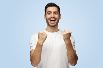 Joyful good-looking man celebrates victory and acts as if he is winner by squeezing fists