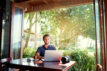 Freelance concept. Professional photographer. Young bearded man using laptop while sitting on summer terrace.