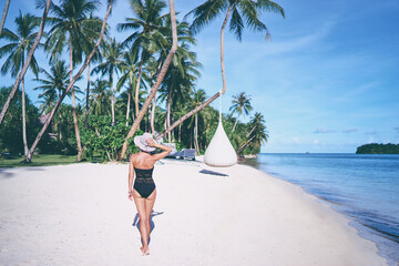 Vacation on the seashore. Back view of young woman walking away on the beautiful tropical white sand beach.