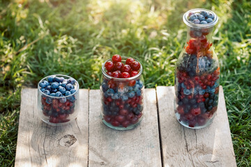 Glassware with different fresh berries on an old wooden bench. Fresh garden berries, blueberry,currant, cherry