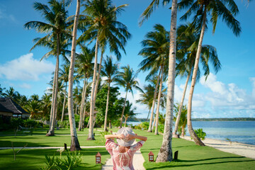 Tropical vacation. Young woman in hat enjoying the view of beautiful coconut palms beach.