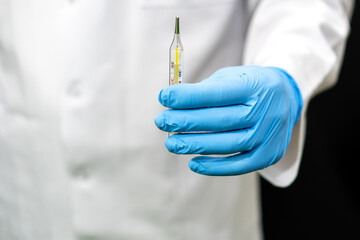 A doctor in blue gloves holds a medical thermometer in his hand. Measurement of body temperature during illness and pregnancy. Mercury medical thermometer close-up.