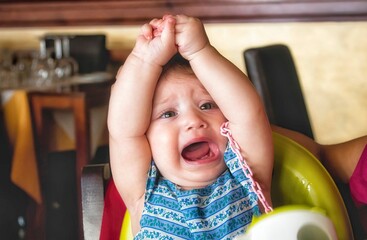 Young child throwing a tantrum in her high chair in a restaurant