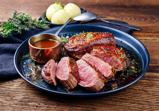Traditionell gegrilltes Gourmet Entenbrust Filet mit Haut serviert mit Kartoffelkn&ouml;del in Dunkelbier Sauce als close-up auf einem rustikalen Metall Tablett