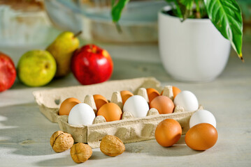 Brown and white chicken eggs in an open cardboard box. preparing breakfast in the morning sun in a kitchen table. mug of coffee, fruits and flowers on the table near the window. easter eggs Close up