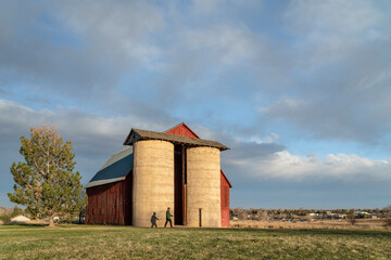 Fototapeta na wymiar male walker at old red barn with twin silo in Colorado foothills, early spring scenery at sunset, public Shenandoah Park in Fort Collins