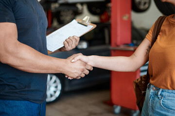 We offer great service and advice. Shot of a woman shaking hands with a mechanic in an auto repair shop.