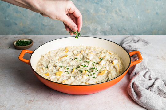 Smoked haddock risotto in a pan being sprinkled with parsley