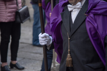 Plano detalle de un hombre desfilando durante una procesión de Semana Santa. Lleva una capa...
