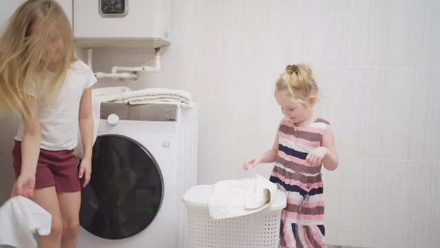 two cute and cheerful girls play with laundry in the laundry room. 