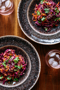 Two plates with red cabbage salad, glass, view from above, on wooden background