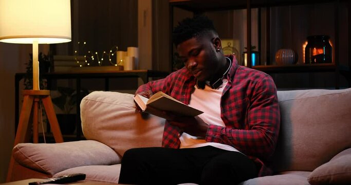 African American man reading a book late night at home