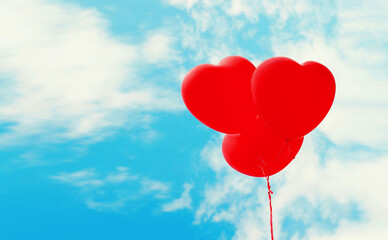 Fototapeta na wymiar Bunch of red heart shaped balloons flying on blue sky background