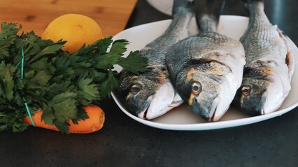 Three fresh ready to cook raw bream fish dorado laying on a plate with ingredients and carrot top. High quality photo