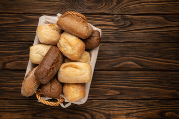 Fresh wheat and rye bread in a wicker basket on a brown wooden table