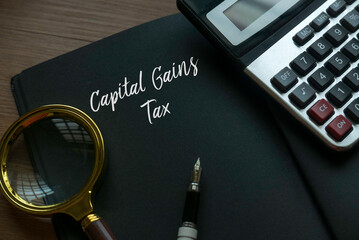 Magnifying glass, pen, calculator and notebook written with Capital Gains Tax. Business and finance...