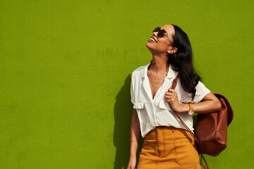 Fototapeta premium Staying stylish is important to me. Cropped shot of an attractive young woman wearing sunglasses while standing alone against a green background in the city.