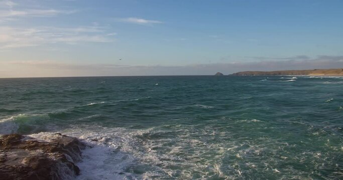 View of Ocean from Southwest Coast Path Cliff Edge towards Rock Formations Drenched in Golden Sunlight, Perranporth, Cornwall, England, United Kingdom - panning shot
