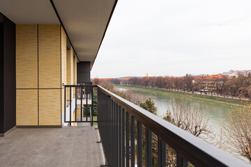 Wide balcony of a multi-storey building with stylish metal black railings. The balcony overlooks the river.