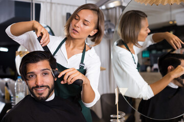 female professional shaving cheerful male's hair in hairdressing salon