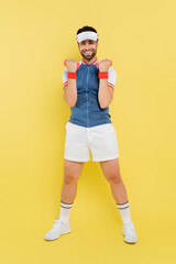 Full length of happy sportsman working out with dumbbells on yellow background.
