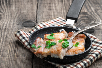 Fried pork slices in frying pan on wooden table