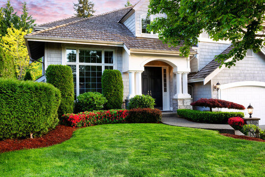 Beautiful home exterior in evening with healthy green lawn and flowerbeds
