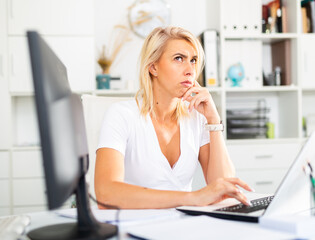 Upset woman working with laptop and papers at the office